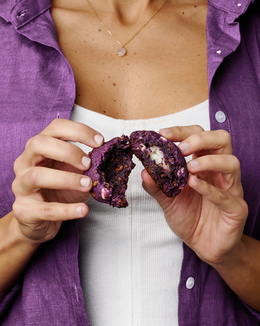 Woman wearing a purple button-down over white tank. Her hands are splitting a cookie in half so the mochi and corn flakes on the inside can be seen. Image shot by Megan Morello, San Diego and Southern California Food and Photographer.
