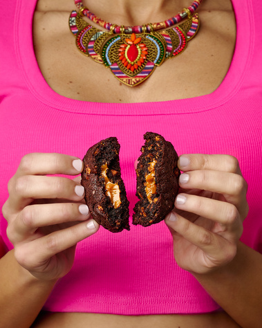 Woman wearing fuchsia crop top and colorful necklace. Her hands are splitting a cookie in half so the filling inside can be seen. Image shot by Megan Morello, San Diego and Southern California Food and Photographer.