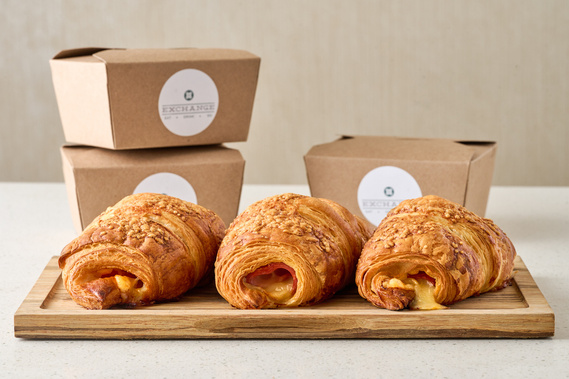 Three ham and cheese croissants on wooden cutting board. Cheese oozing from ends of croissant. Image by Megan Morello Commercial food photographer and lifestyle photographer in San Diego, Southern California.