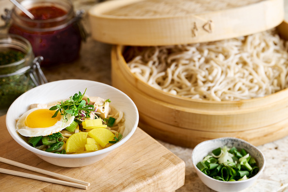 Bowl of ramen in foerground topped with fried egg and sprouts. Basket of noodles and various sauces in mid and background.
Image by Megan Morello Commercial food photographer and lifestyle photographer in San Diego, Southern California.