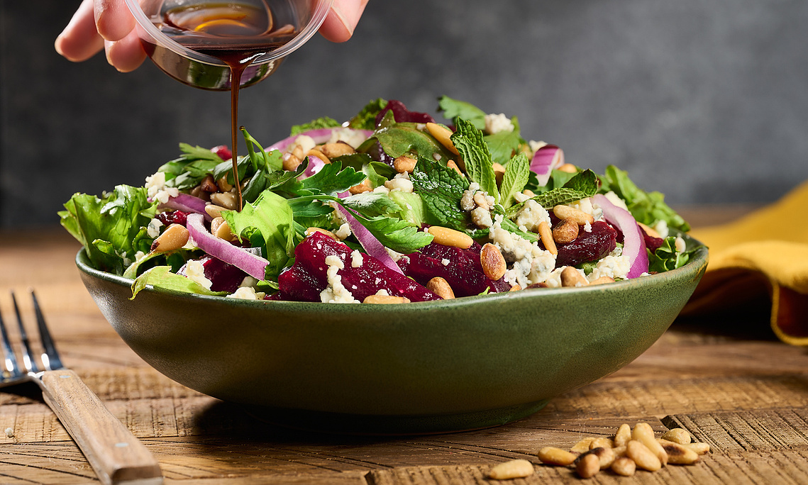 Beet salad in green bowl. Hand visible pouring vinaigrette into salad. Stream of vinaigrette is frozen and in focus. Image by Megan Morello San Diego Food and Lifestyle Photographer.