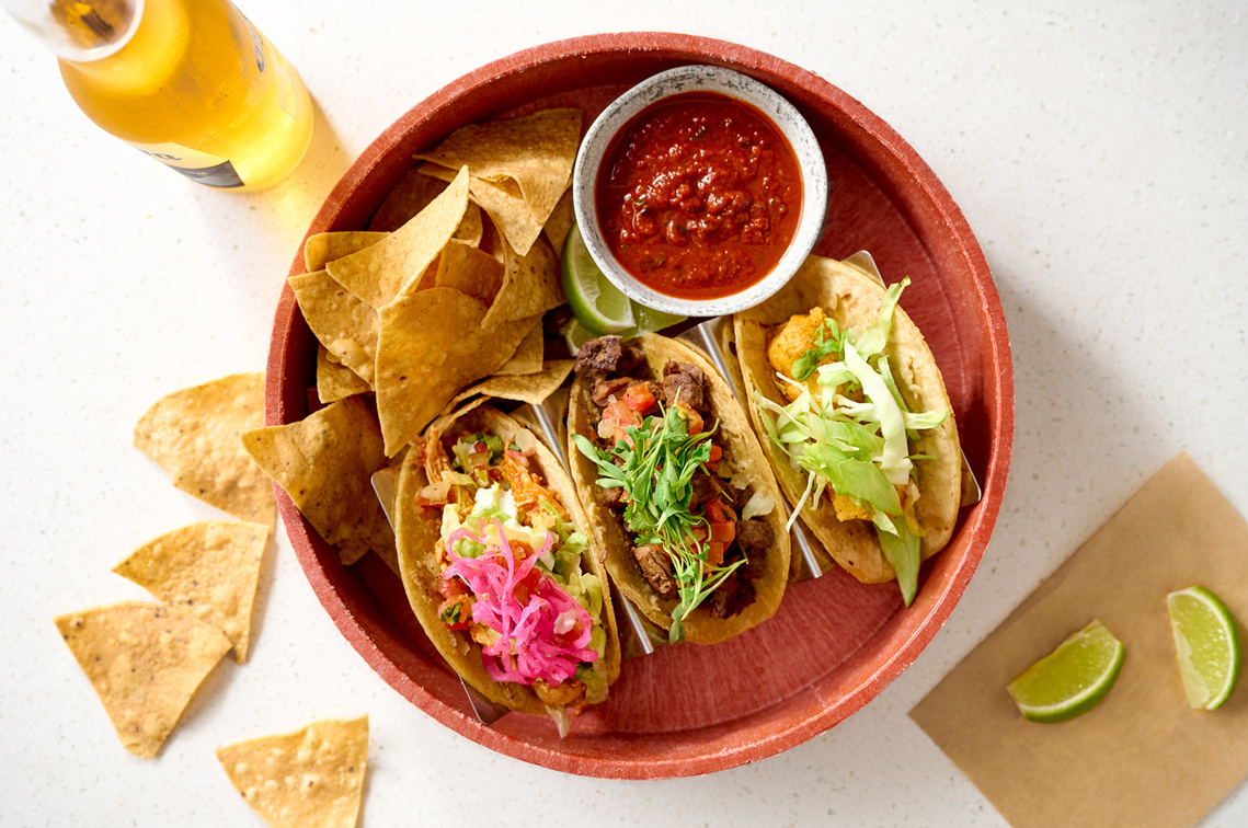 Overhead shot of taco plate. Bright and colorful with chips and lime wedges spilled artfully onto tabletop. Bottle of corona beer.
Image by Megan Morello Commercial food photographer and lifestyle photographer in San Diego, Southern California.