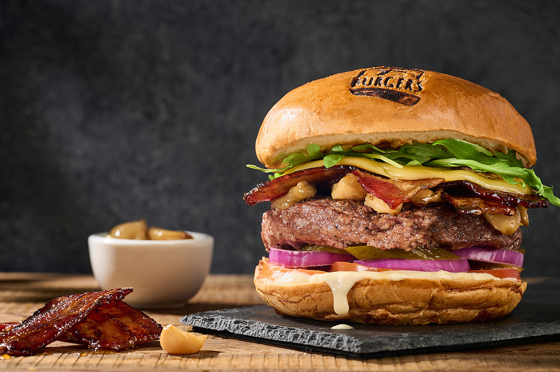 Large Burger with maple infused bacon and roasted garlic. Sauce is dripping on to slate tray where burger is placed. Image by Megan Morello San Diego Food and Lifestyle Photographer.