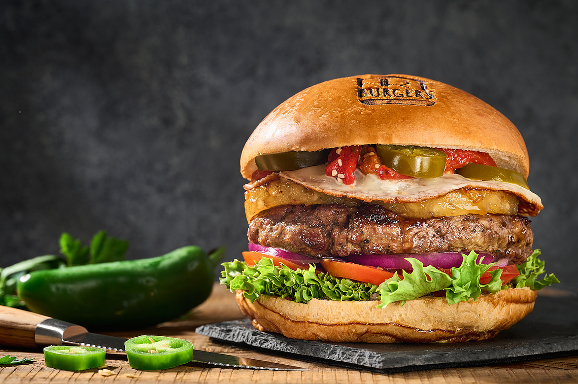 Tall thick hamburger on slate board with unusual toppings of an egg, pineapple, and jalapeños. Image by Megan Morello San Diego Food and Lifestyle Photographer.