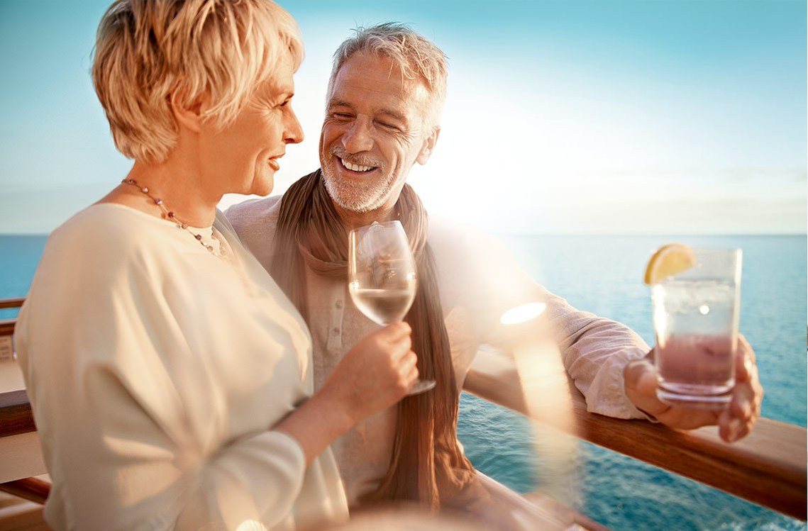 Ein Paar Mitte 50 steht an der Reeling und genießt Wein und Cocktails