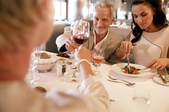 Drei Personen sitzen an einem edel eingedeckten Tisch und stoßen mit einem Glas Wein an
