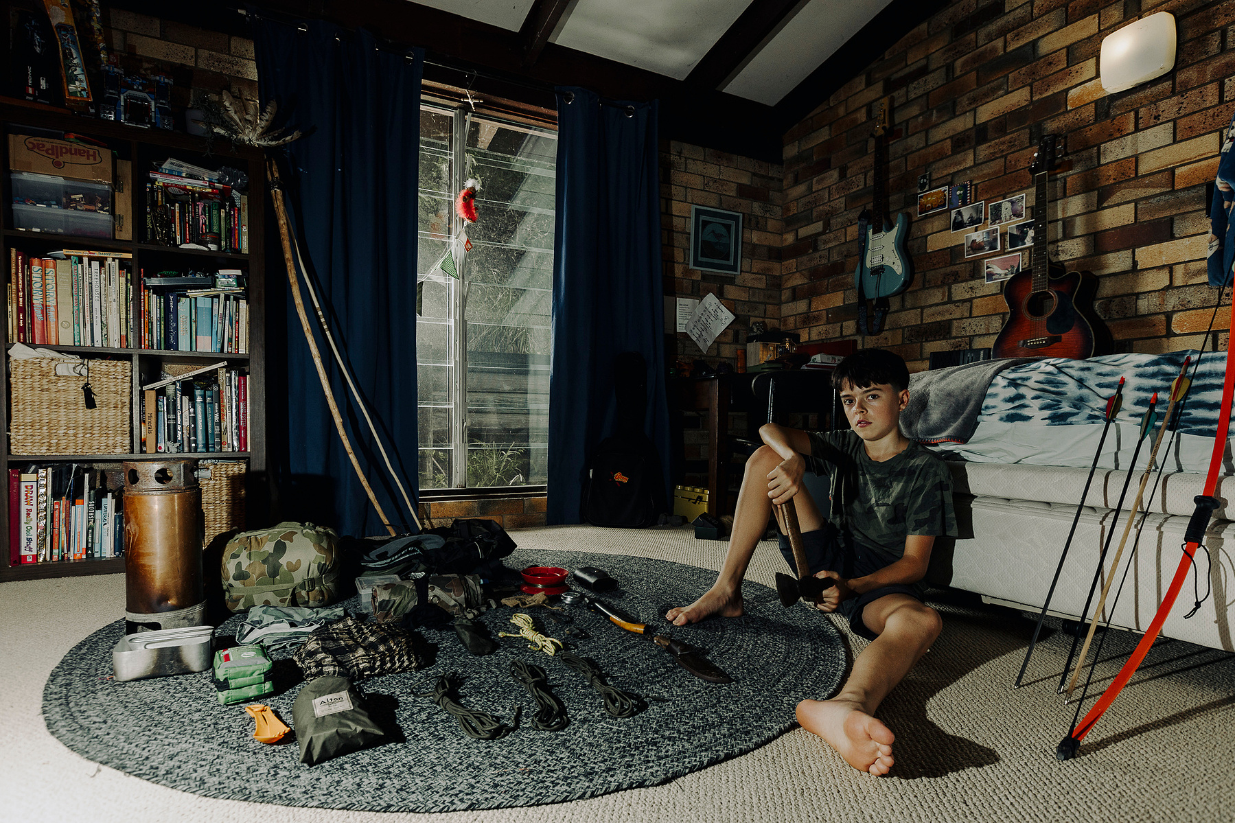 Adolescent boy sitting on the floor in his room with survival gear