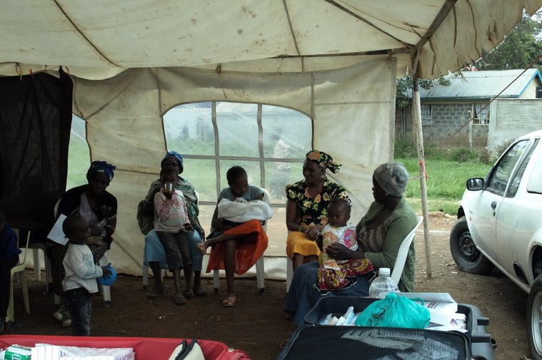 Photo of local women sitting in a marquee-style tent in Nairobi slums holding their babies and waiting to be seen by an osteopath during a medical expedition with Divinity Foundation, 2010.  See blog www.katyteasdale.blogspot.com for a full report.