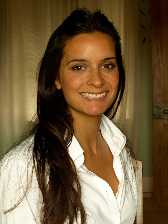 Katy, Registered Osteopath, Consultant Paediatric Osteopath, sits for a colour photographic portrait of her head, shoulders and upper torso angled slightly to the right of the picture as she looks into the camera, smiling. Her hair is long and dark brown.
