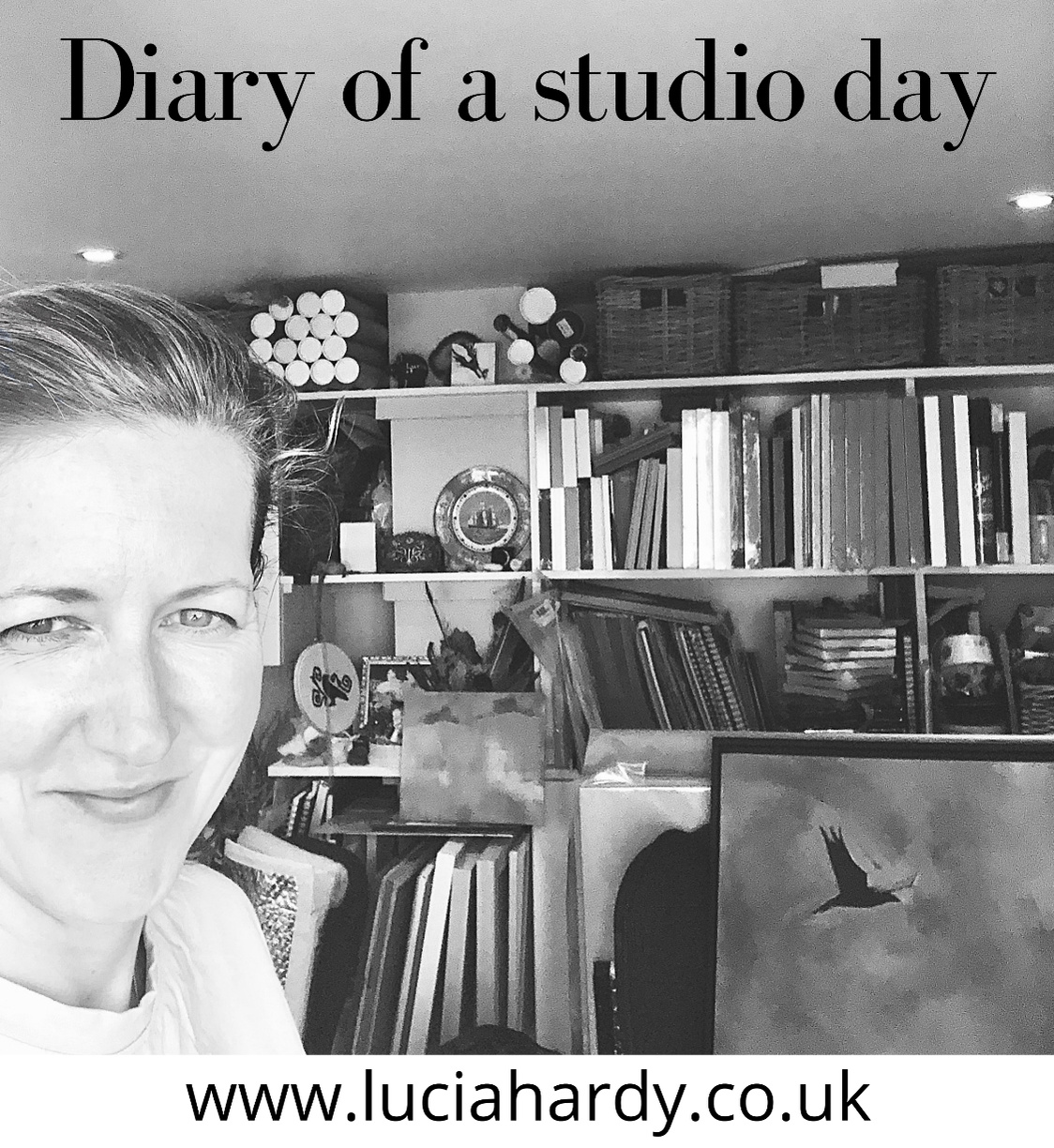 Artist Lucia Hardy standing in her studio, containing frames, canvases and a painting of a crow in the sky.