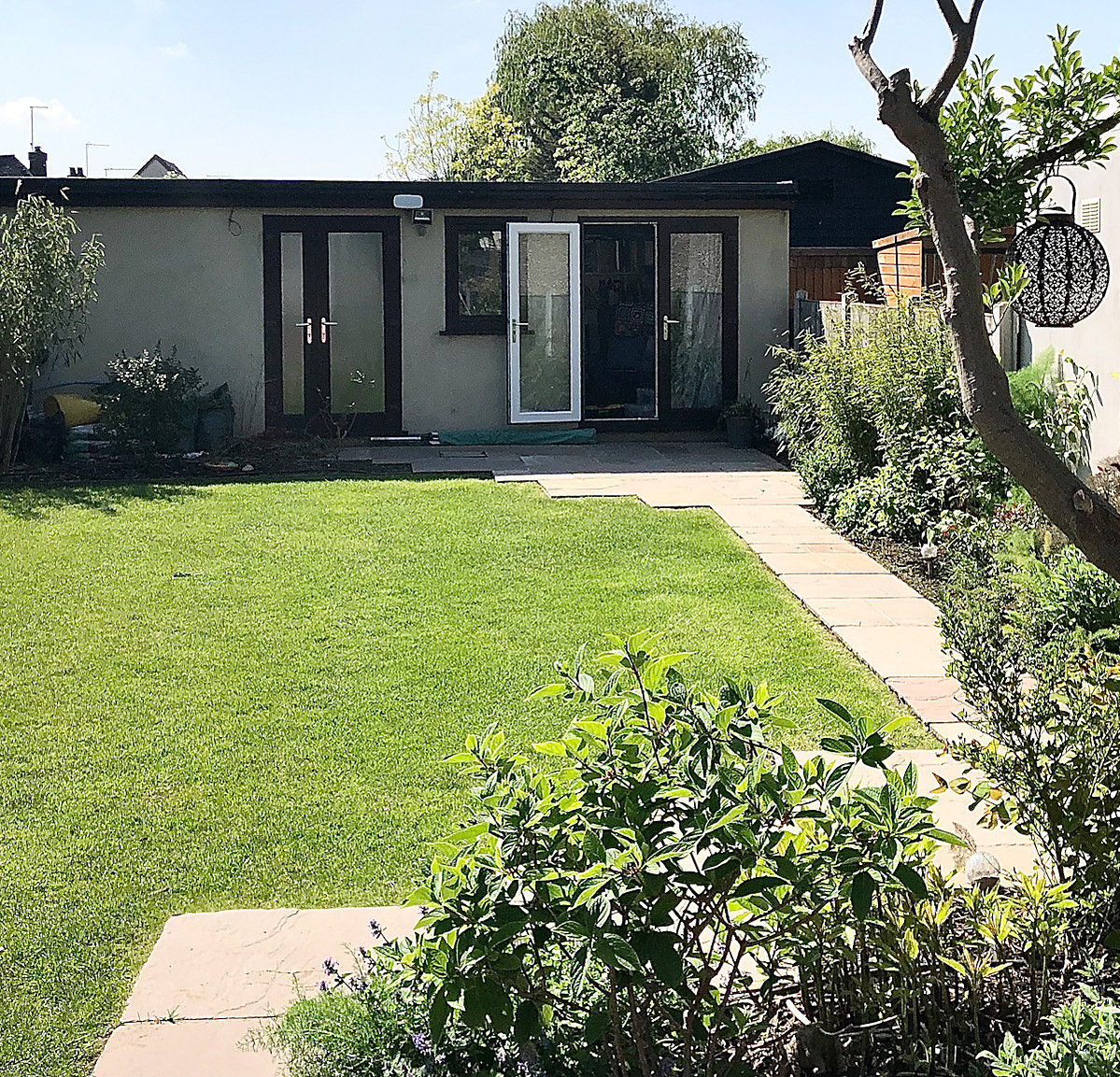 Lucia Hardy's Garden Studio at the end of a  stone path across a green lawn with a messy verdant border.