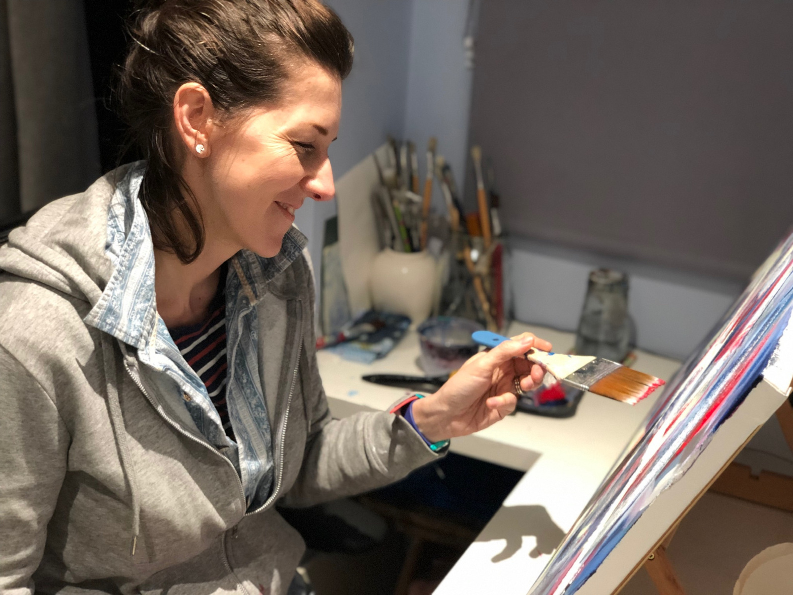 Picture of artist Lucia Hardy painting at a desk easel using a large flat brush on a big canvas.