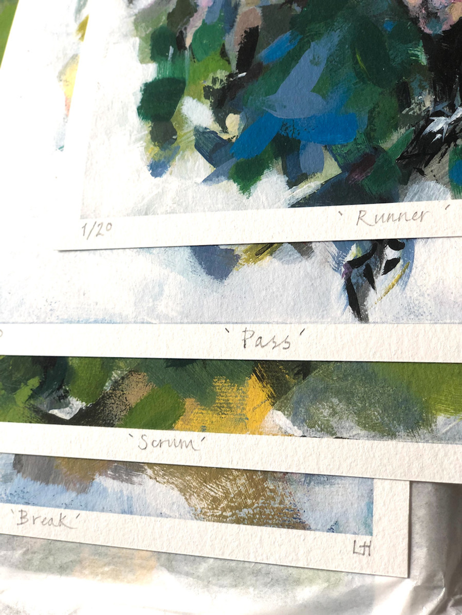 A close up of a pile of limited edition prints, numbered named and signed, with a glimpse of some abstract marks and  colours.