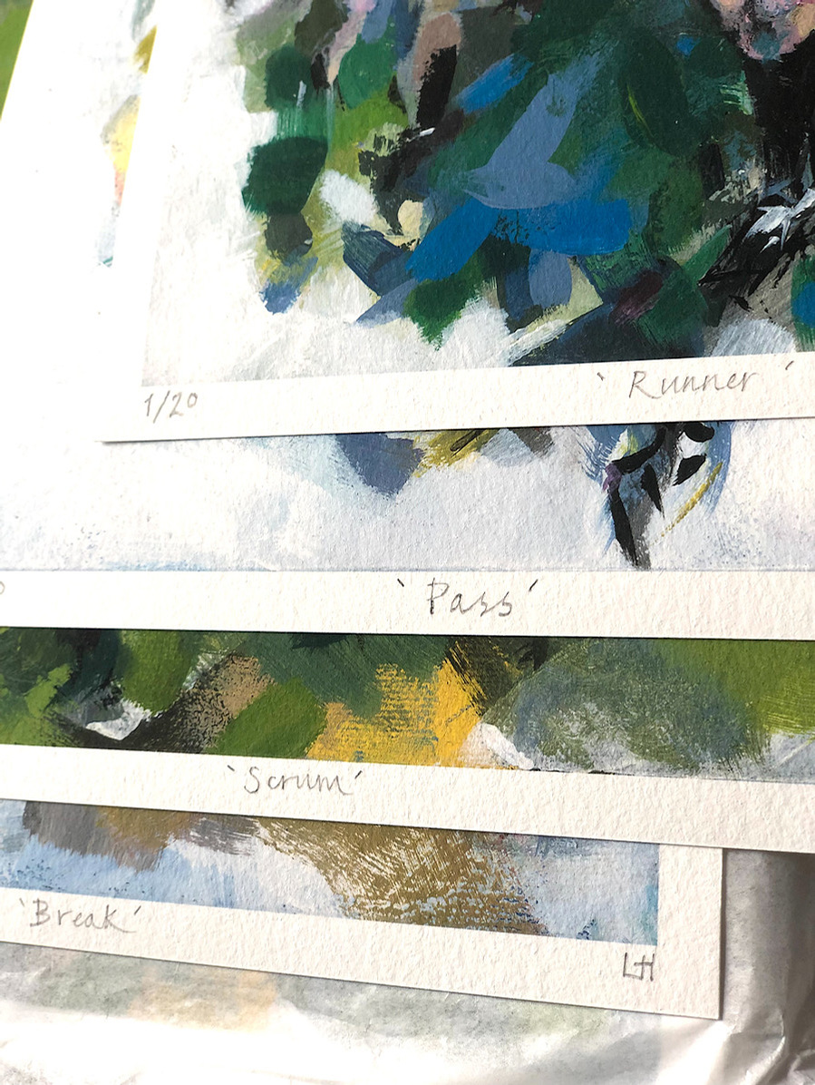 A close up of a pile of limited edition prints, numbered named and signed, with a glimpse of some abstract marks and  colours.