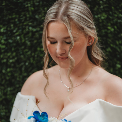 The bride stands in a serene garden, framed by soft, natural light. Her elegant lace gown drapes beautifully to the ground, its intricate details catching the light with every step. Her veil flows gently behind her, creating a soft, ethereal aura. Her bou