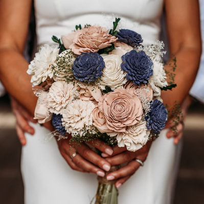 The bridal bouquet bursts with vibrant colors, a perfect mix of delicate blooms and lush greenery. At its center, soft blush roses are paired with ivory peonies, surrounded by sprigs of eucalyptus and baby's breath, adding texture and depth. Hints of lave