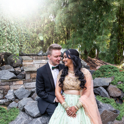 Bride and groom sit on rocks to pose before reception 