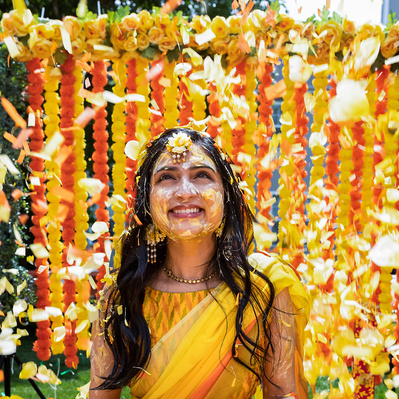 Bride being showered with yellow and orange flowers during haldi ceremony