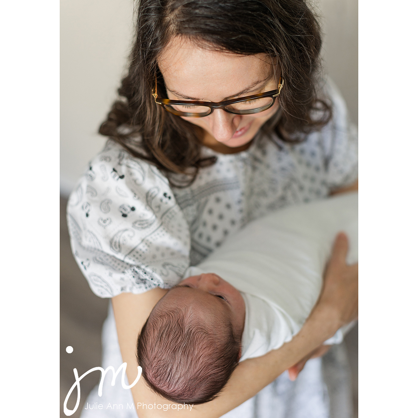 New mother and newborn child wrapped in white blanket, looking at one another.