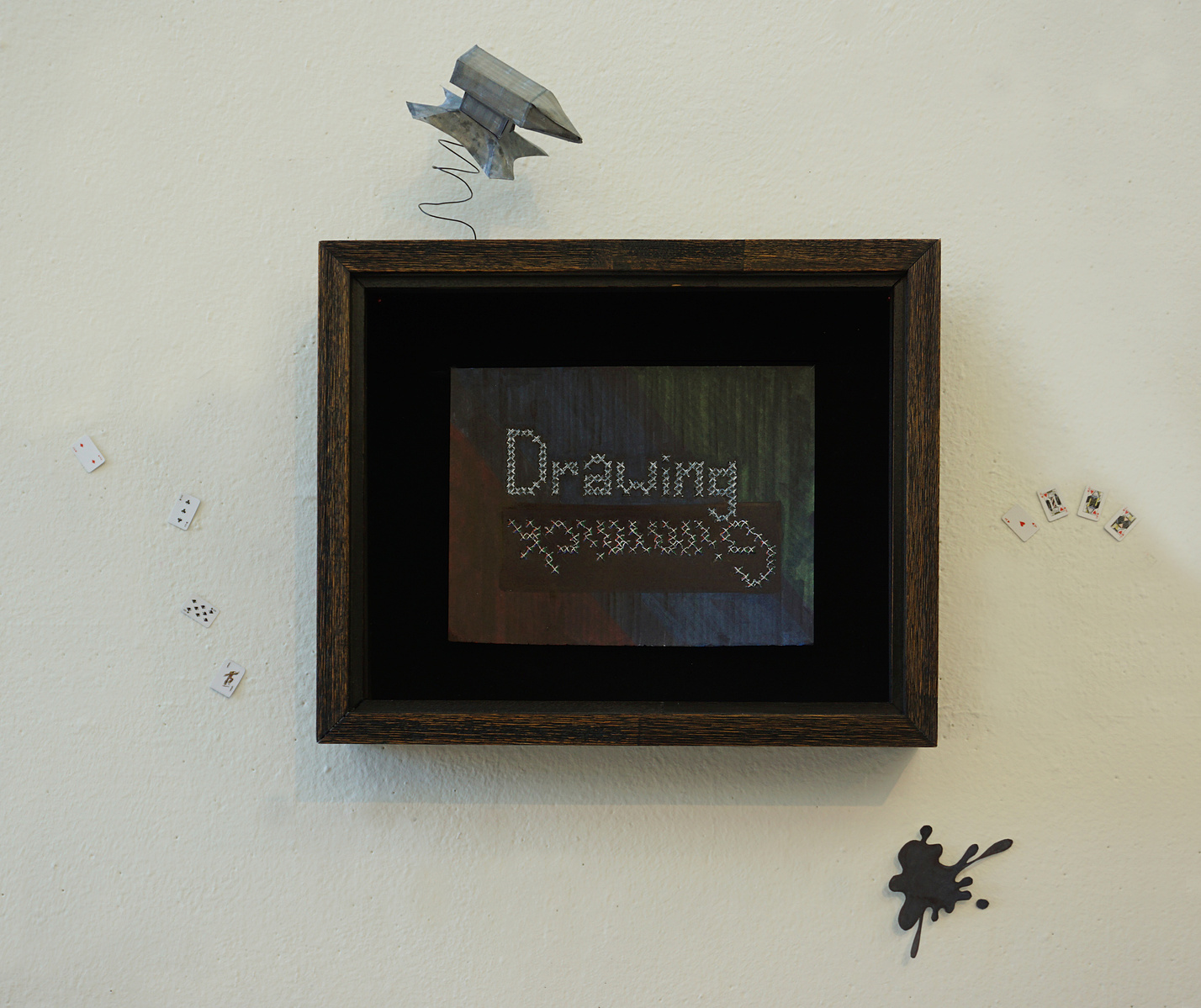 a funny piece of art in a shadow box with an anvil, splat mark, and playing cards