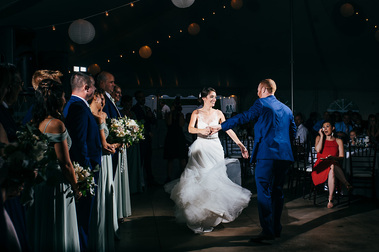 A bride twirls and dances with her groom during their White Mountains wedding ceremony in New Hampshire, bathed in light against a dark background