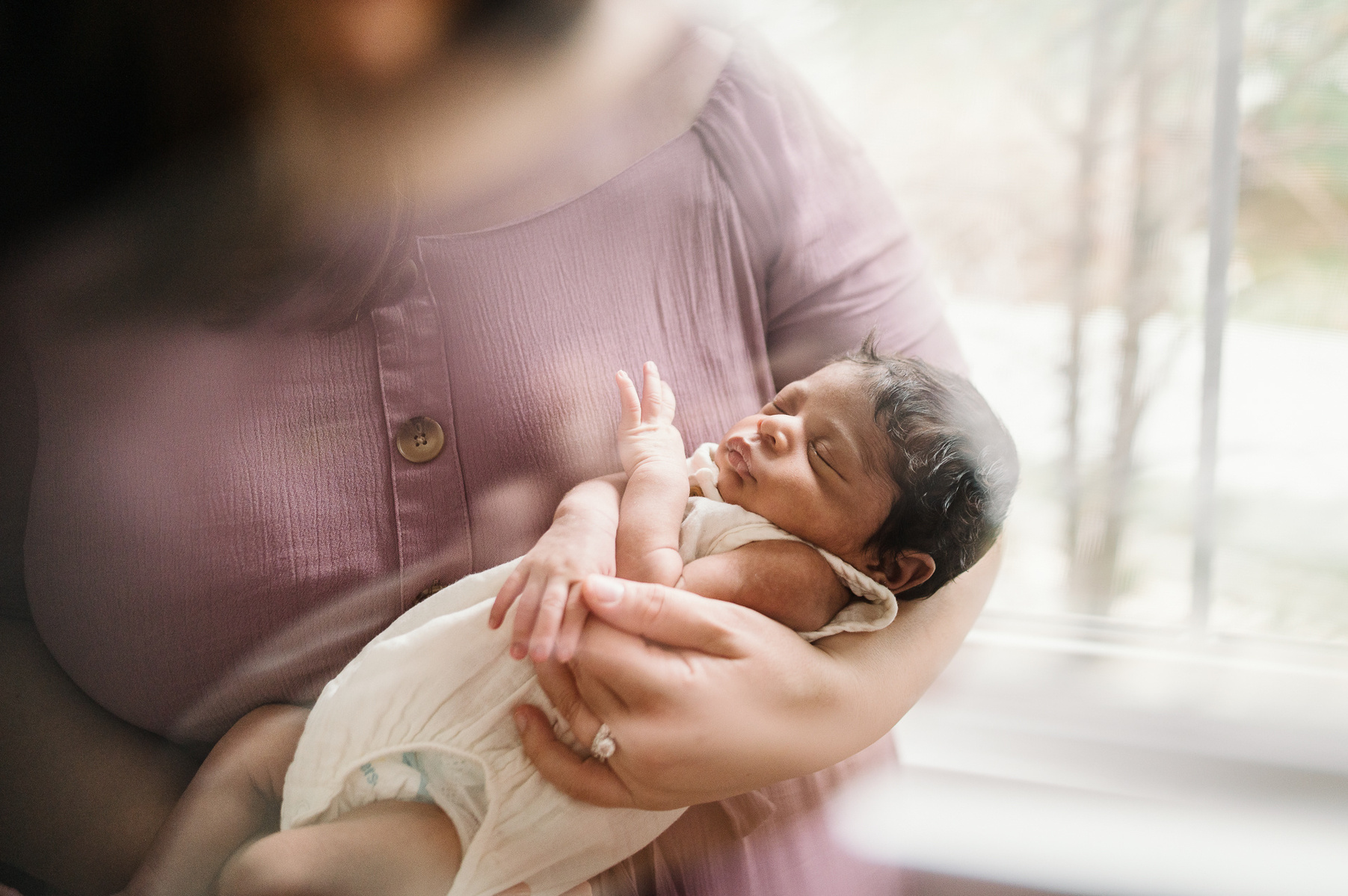a newborn is held against the soft pink dress of her mother during their boston newborn photography session