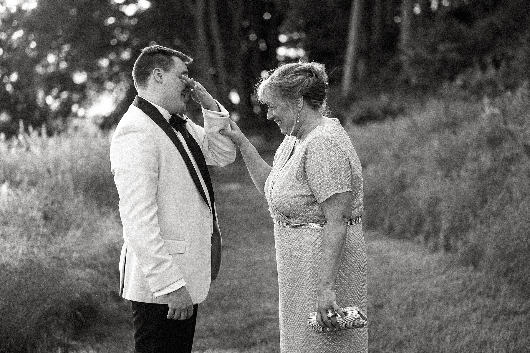A groom starts crying while his mother lovingly looks on and laughs and comforts him with a touch