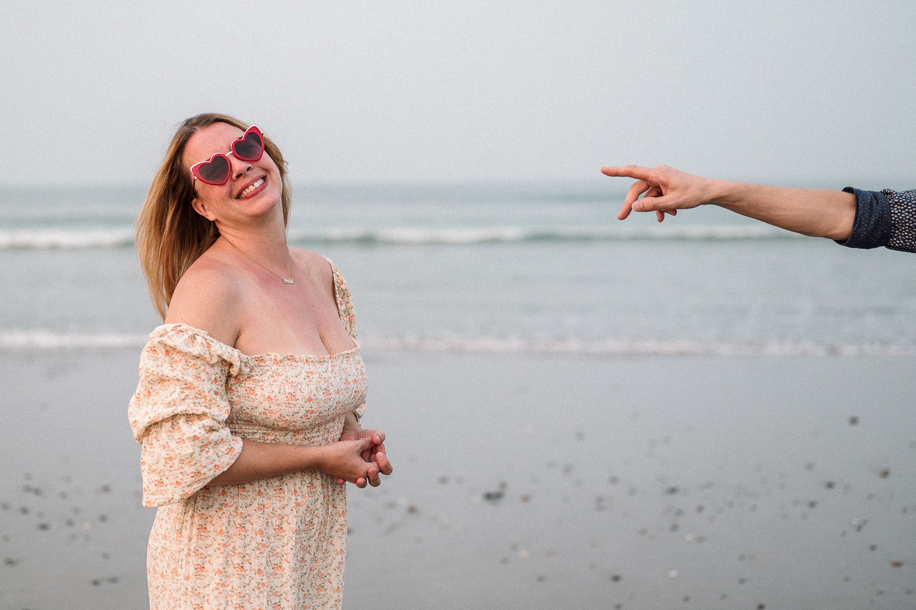 An arm points at a woman in heart shaped sunglasses at their nantasket beach engagement session by Korri Leigh Photography