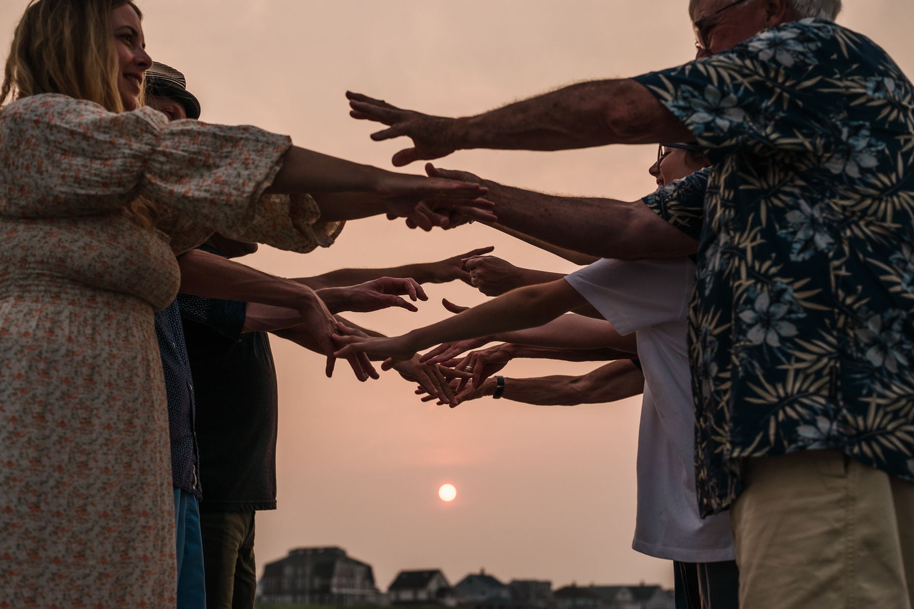 a family extended their arms towards each other in front on a bright pink sunset caused by the canadian wildfires during their nantasket beach family photography session