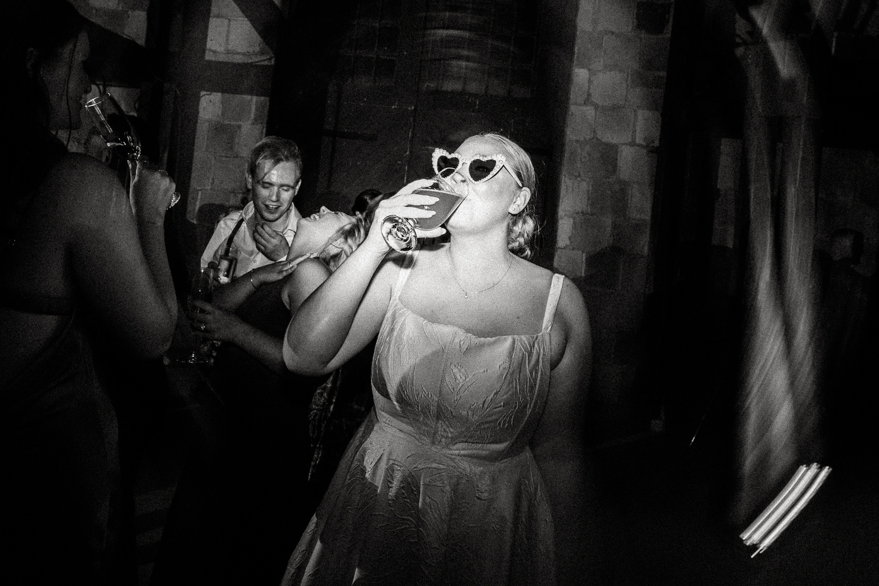 A bride wearing heart-shaped sunglasses dances and drinks at her Barn at the Crane Estate wedding reception