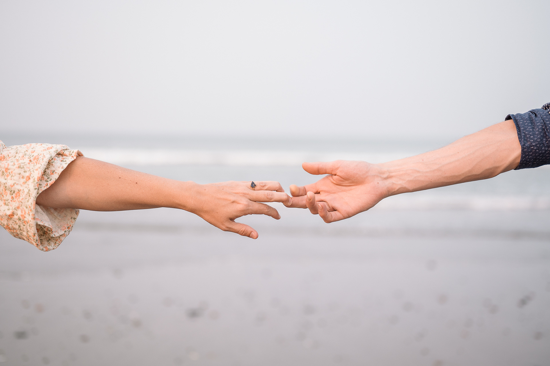 Two hands reach towards each other isolated in front of the Atlantic ocean at a nantasket beach engagement session by Korri Leigh Photography