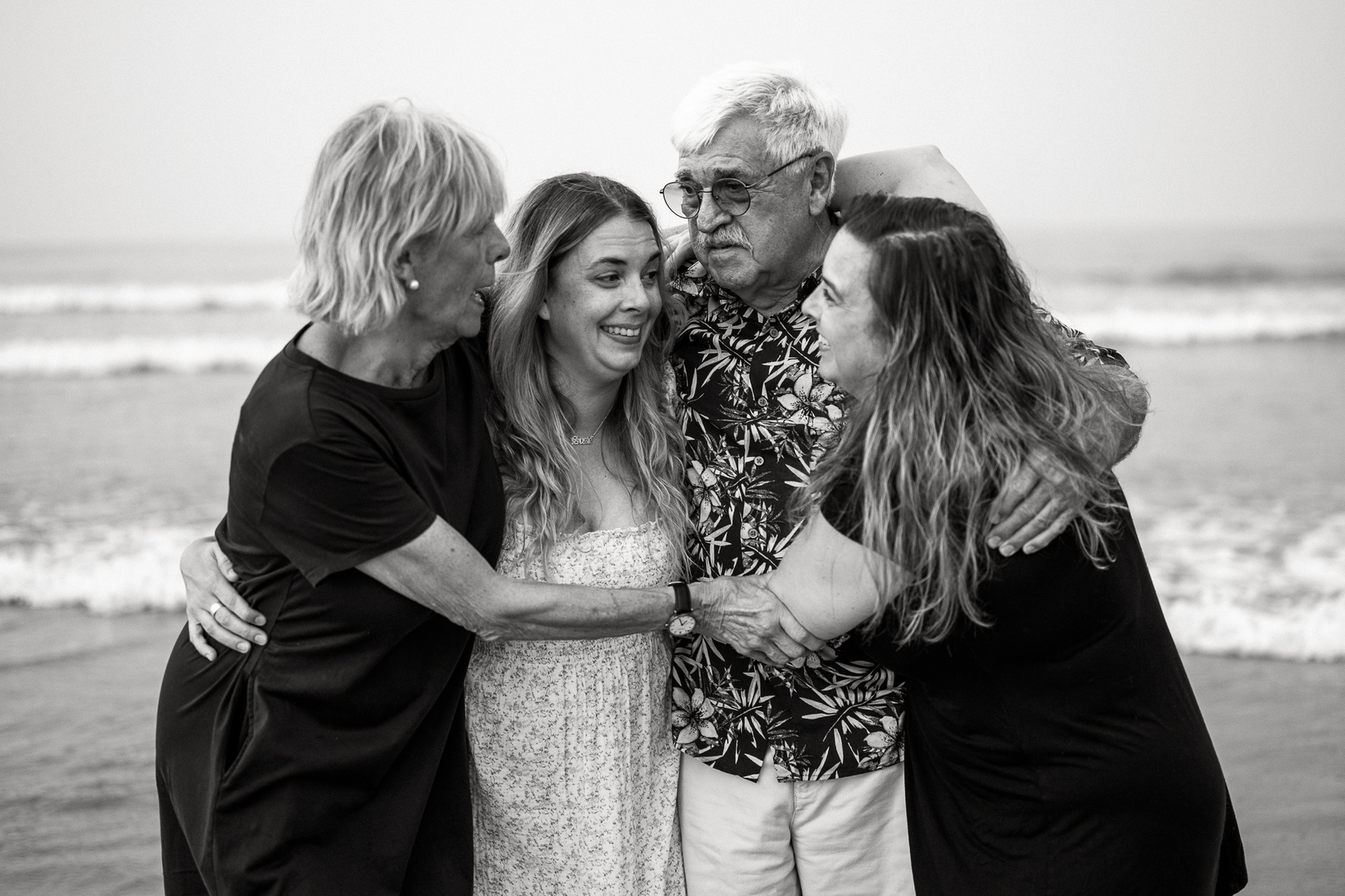A family stands comfortably and smiles in black and white on Nantasket Beach at their Hull family photography session by Korri Leigh Photography