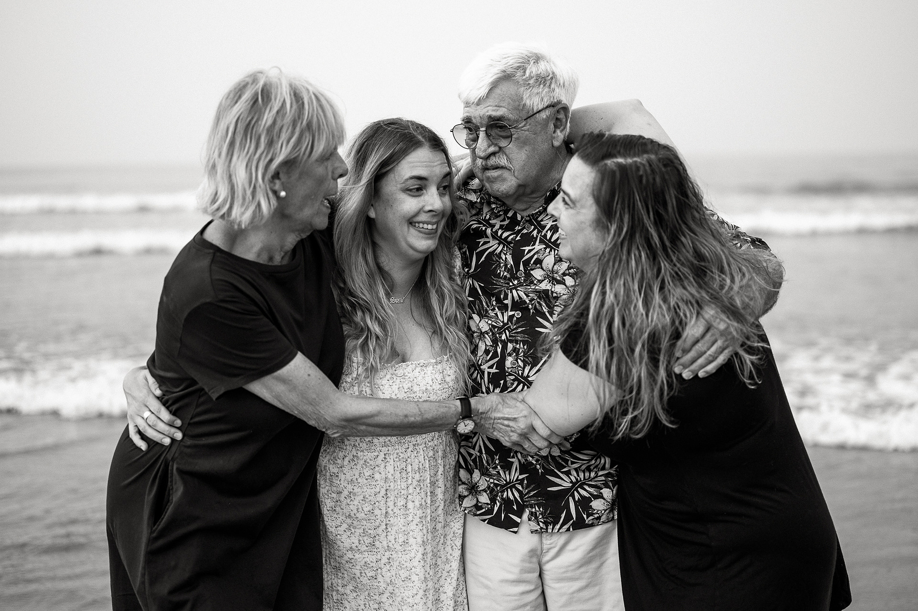 A family stands comfortably and smiles in black and white on Nantasket Beach at their Hull family photography session by Korri Leigh Photography