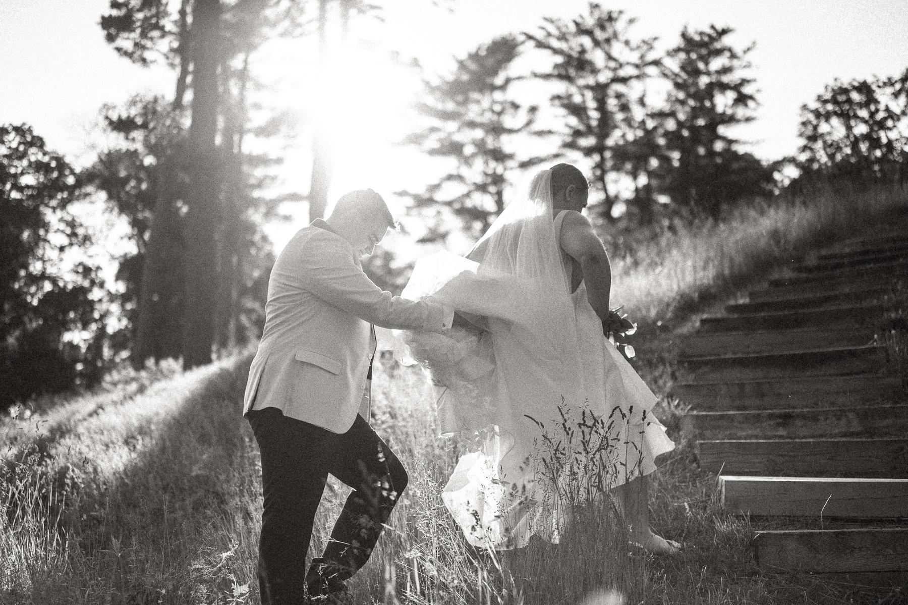 A groom holds the dress of his bride while walk in golden sunlight down the steps of Castle Hill on the ground of the Crane Estate in Ipswich MA
