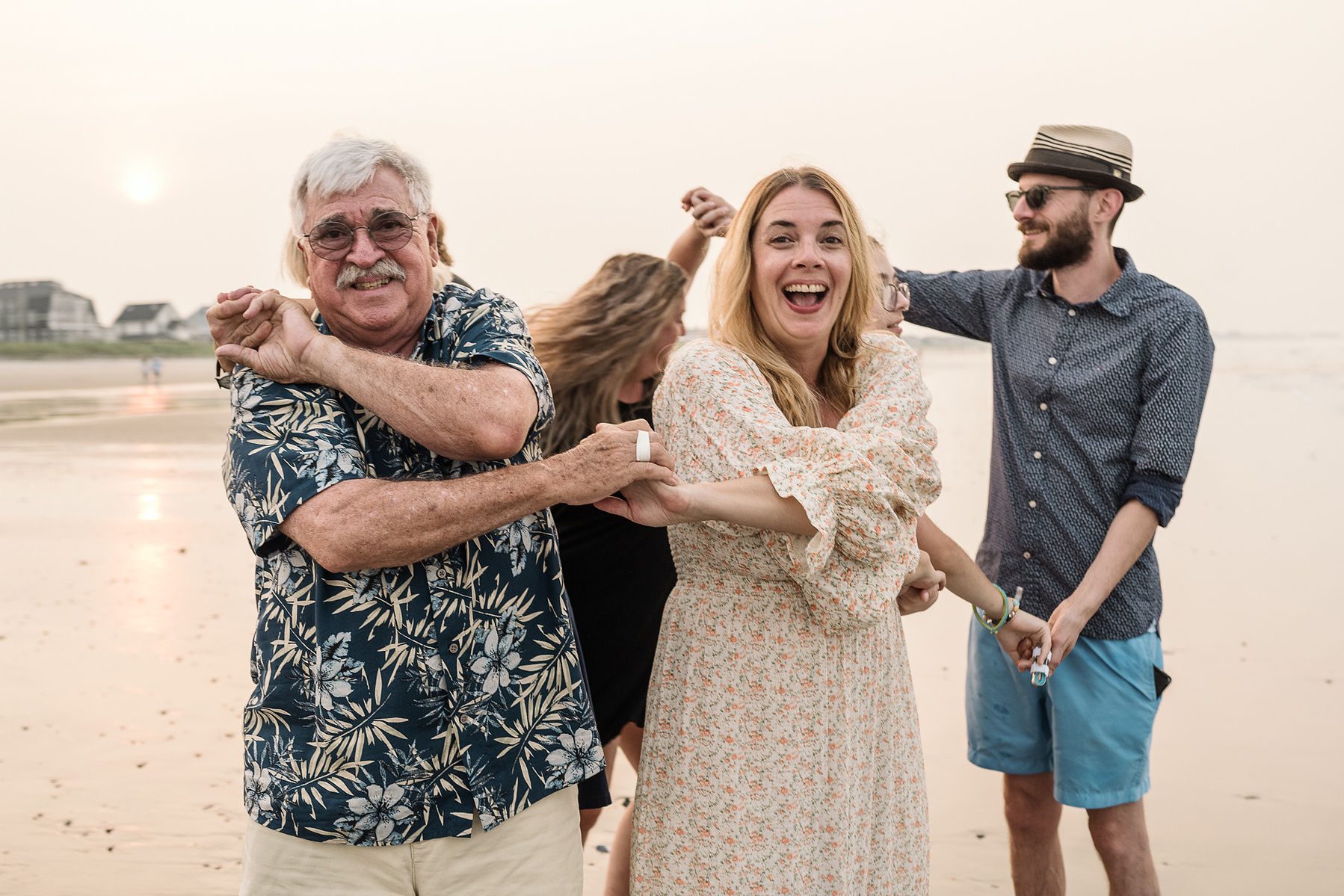 A family stands with their arms intertwined and smiles on Nantasket Beach at their Hull family photography session by Korri Leigh Photography