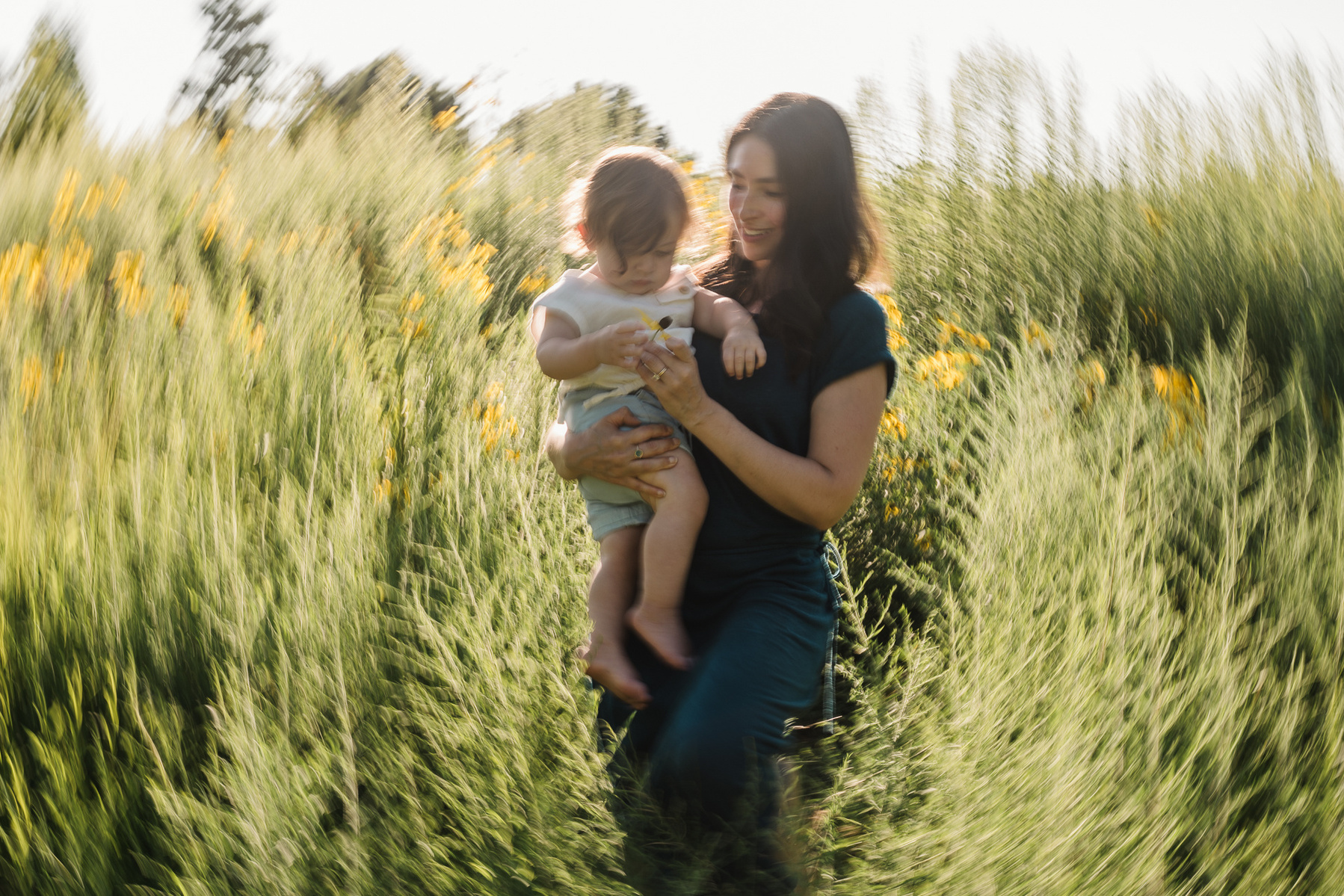 A mother and her baby son walk through a field in the sunshine at Fisher Hill Reservoir Park in Brookline MA