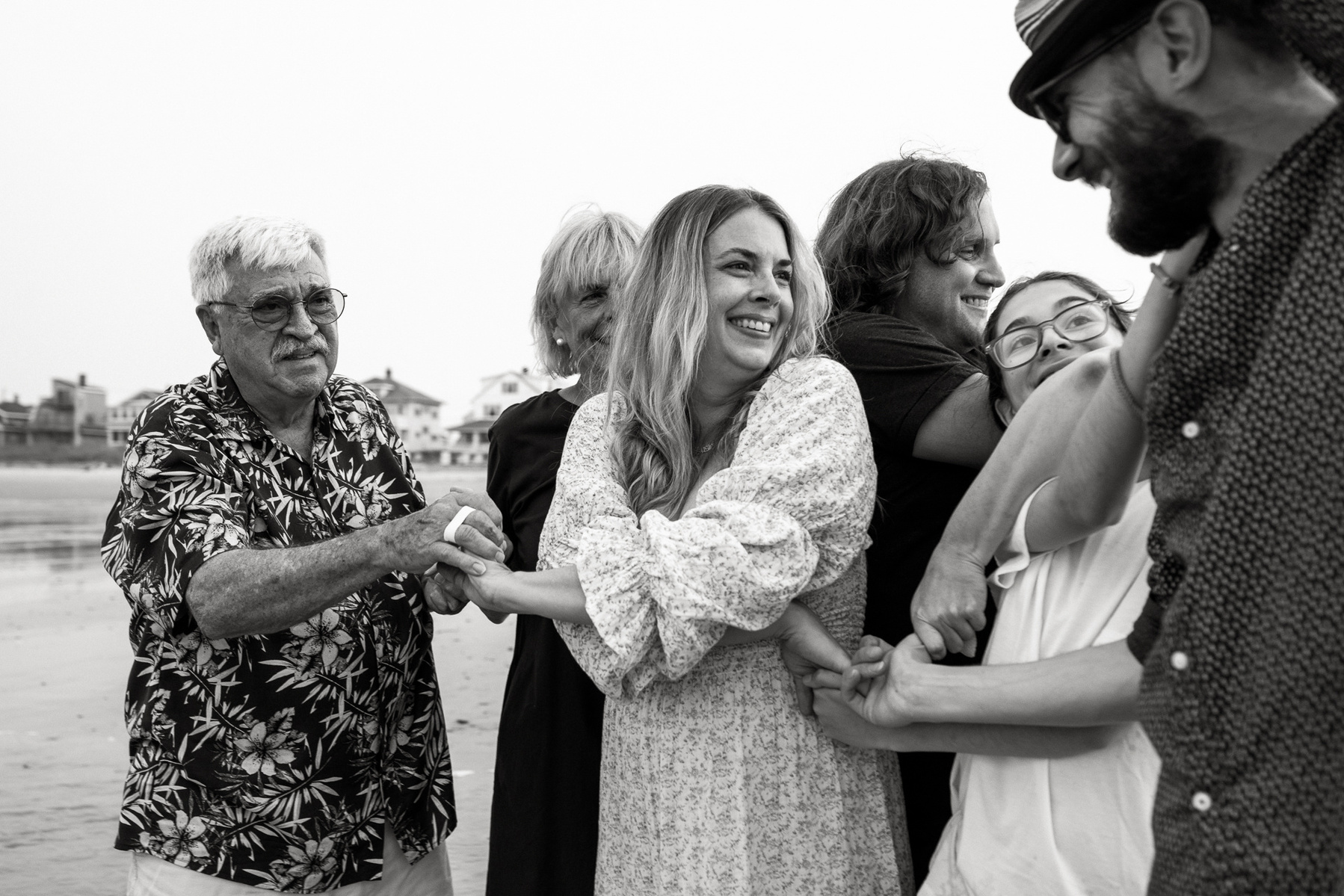 A family stands with their arms intertwined and smiles on Nantasket Beach at their Hull family photography session by Korri Leigh Photography