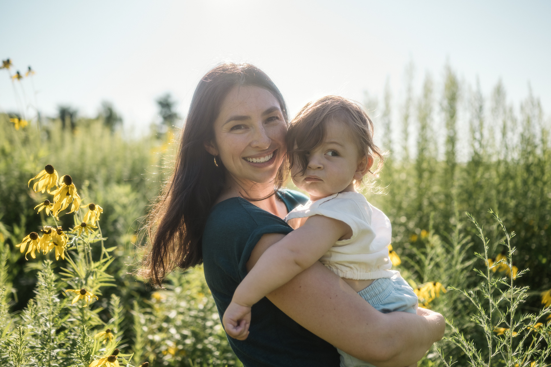 A mother and her baby smile in a field at Fisher Hill Reservoir Park in Brookline MA