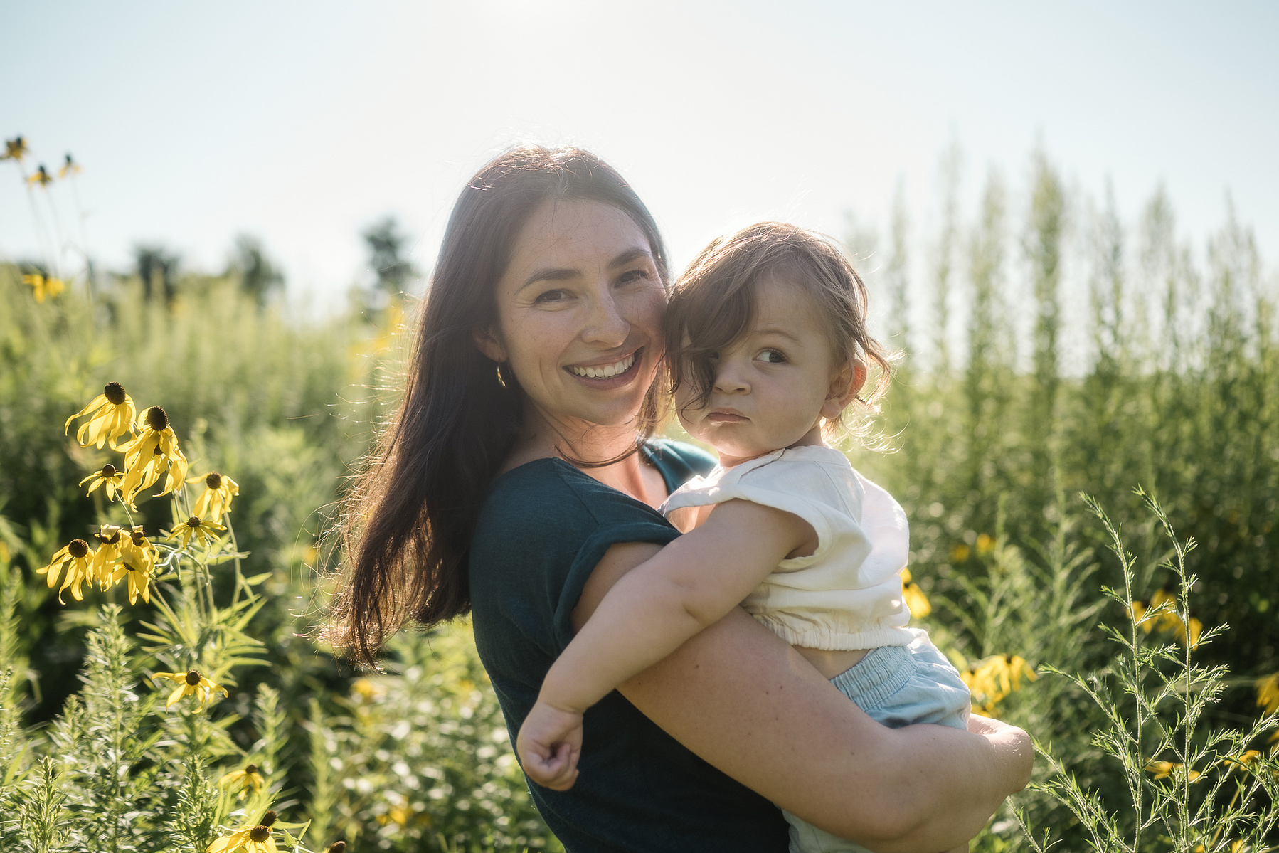 A mother and her baby smile in a field at Fisher Hill Reservoir Park in Brookline MA