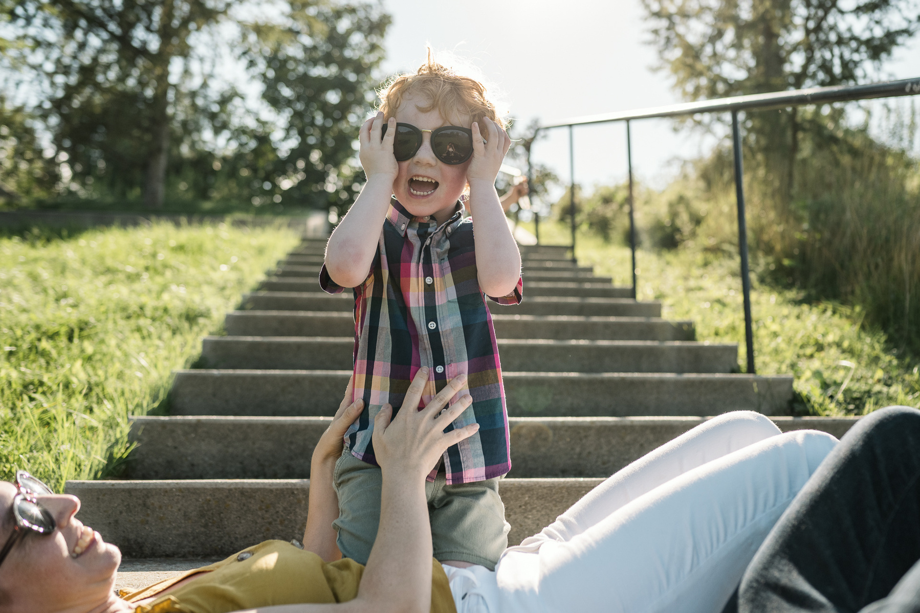 A kid plays with sunglasses on in the light of the stairs at Fisher Hill Reservoir Park in Chestnut Hill by Brookline family photographer Korri Leigh Photography
