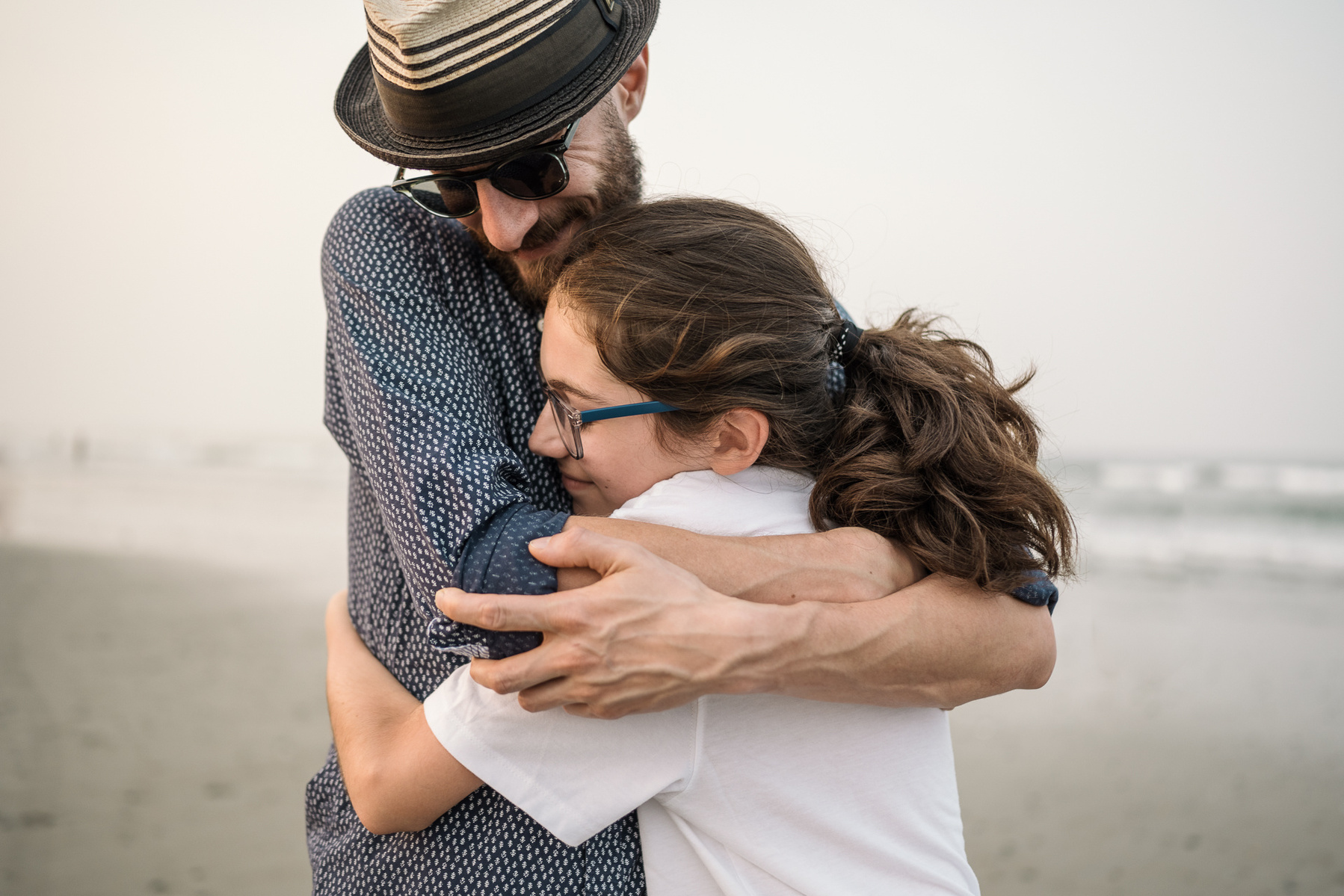 A father in a hat hugs his son on Nantasket Beach at their Hull family photography session by Korri Leigh Photography