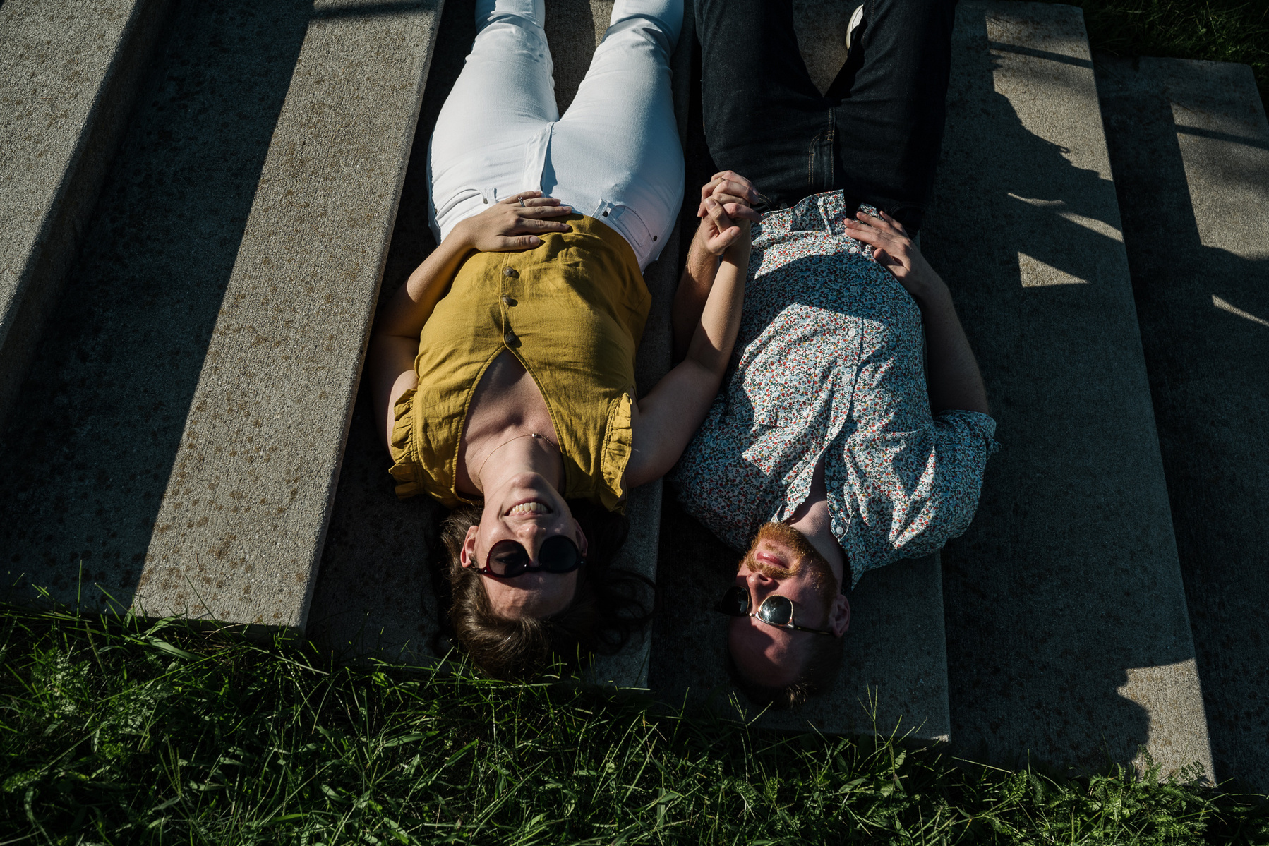A couple with sunglasses on lays in the light of the stairs at Fisher Hill Reservoir Park in Chestnut Hill by Brookline family photographer Korri Leigh Photography