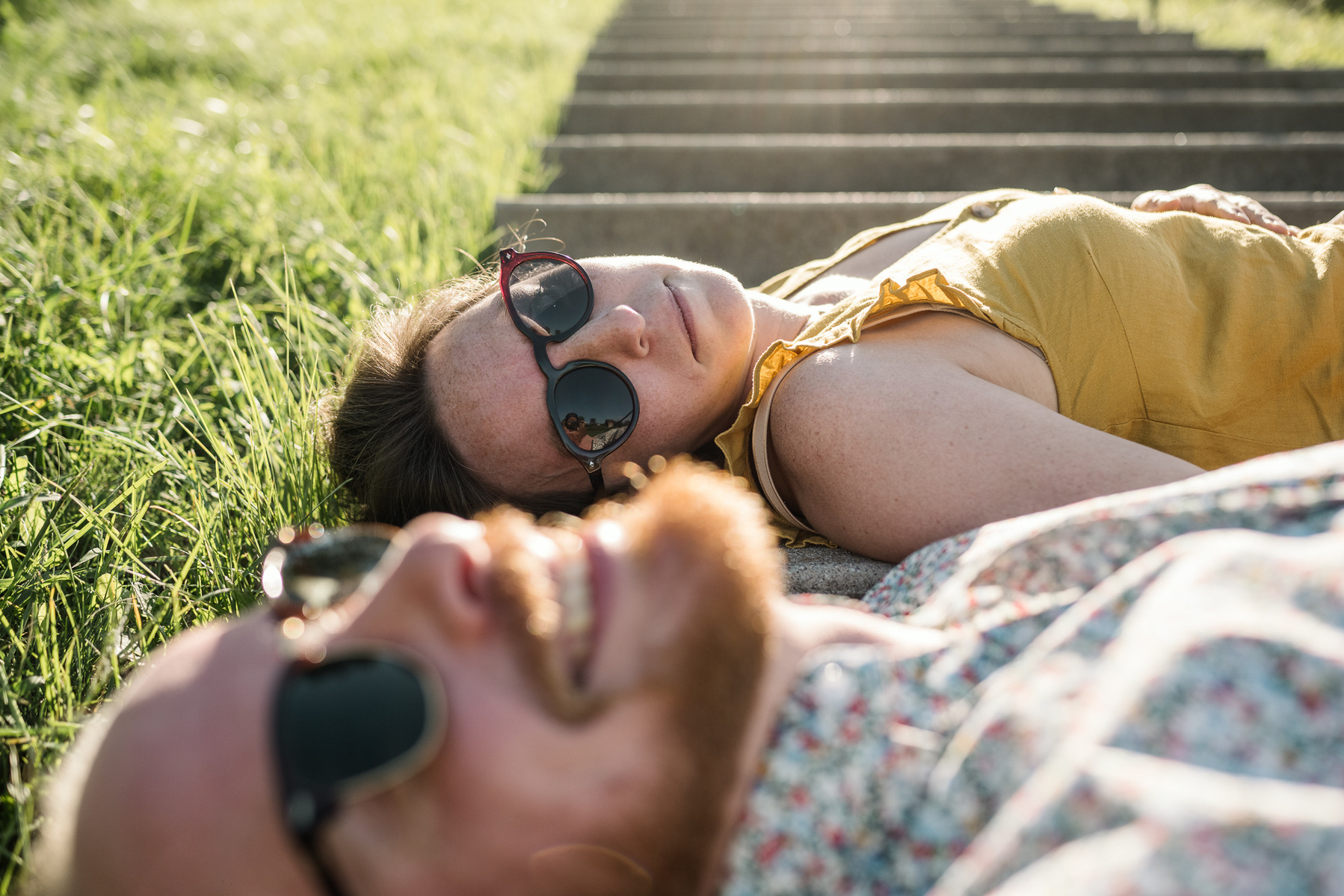 A couple with sunglasses on lays in the light of the stairs at Fisher Hill Reservoir Park in Chestnut Hill by Brookline family photographer Korri Leigh Photography