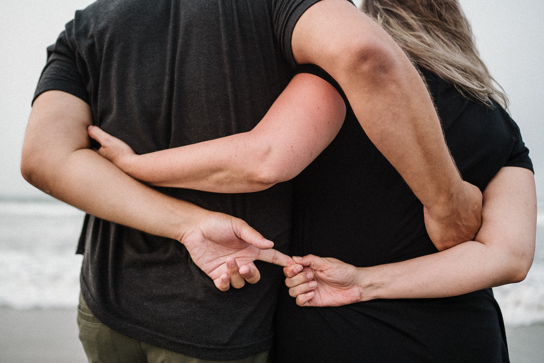 A couple intertwines their arms and hands together on Nantasket Beach at their Hull family photography session by Korri Leigh Photography