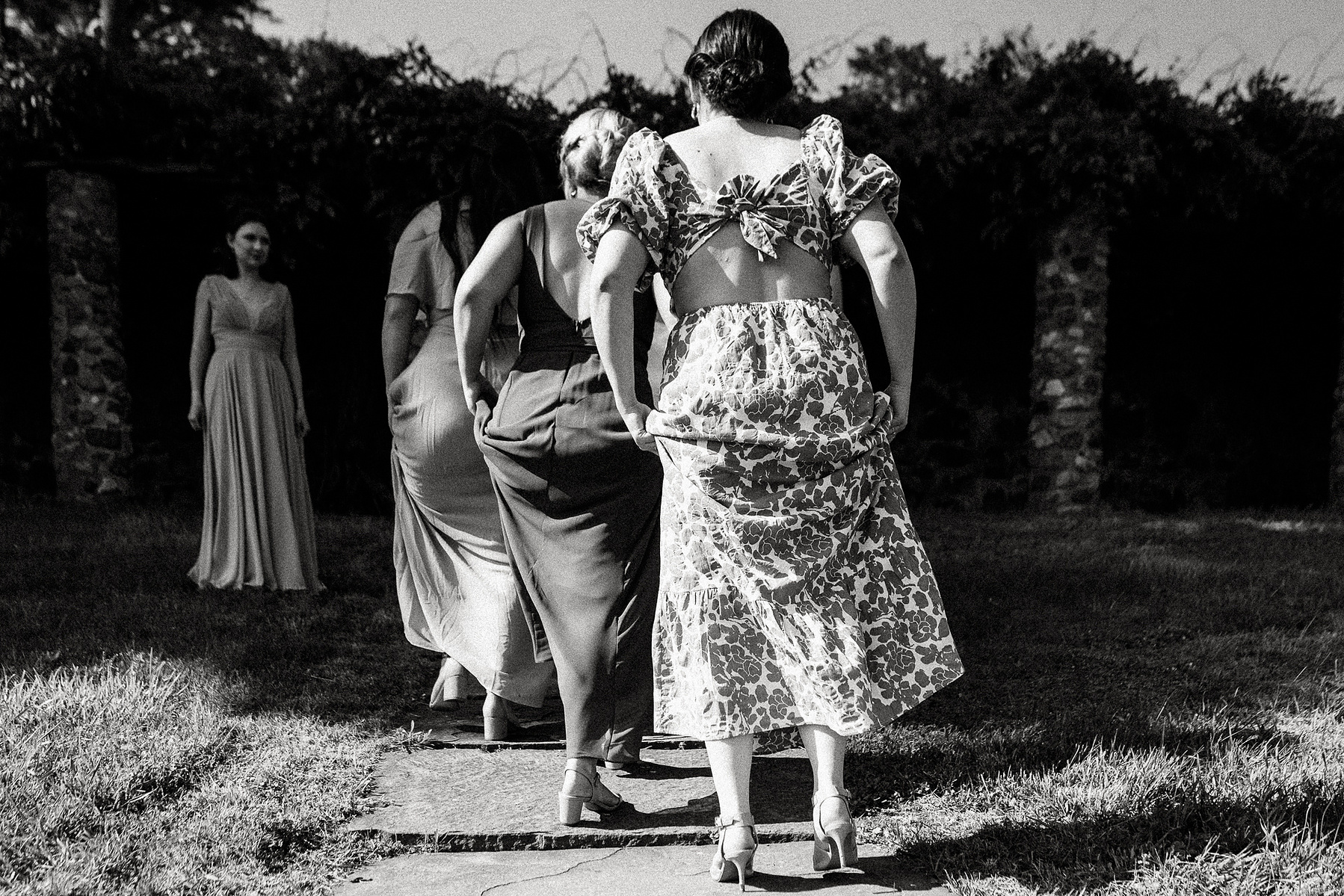 Bridesmaids walk away from the camera, all holding their dresses up in a similar pose