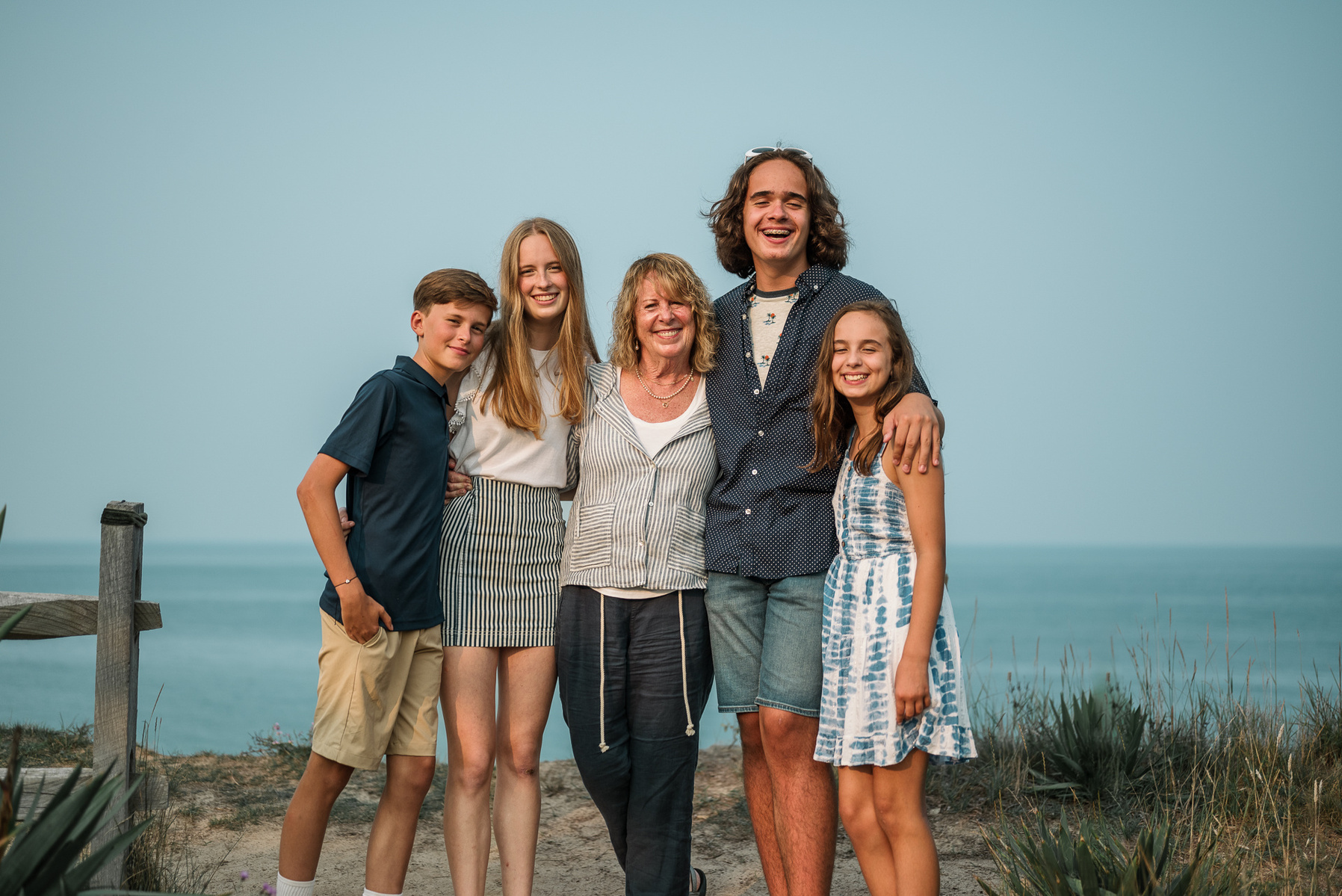 A grandmother smiles and poses while flanked by her 4 grandchildren as they pose at the Nauset Lighthouse in Eastham Massachusetts