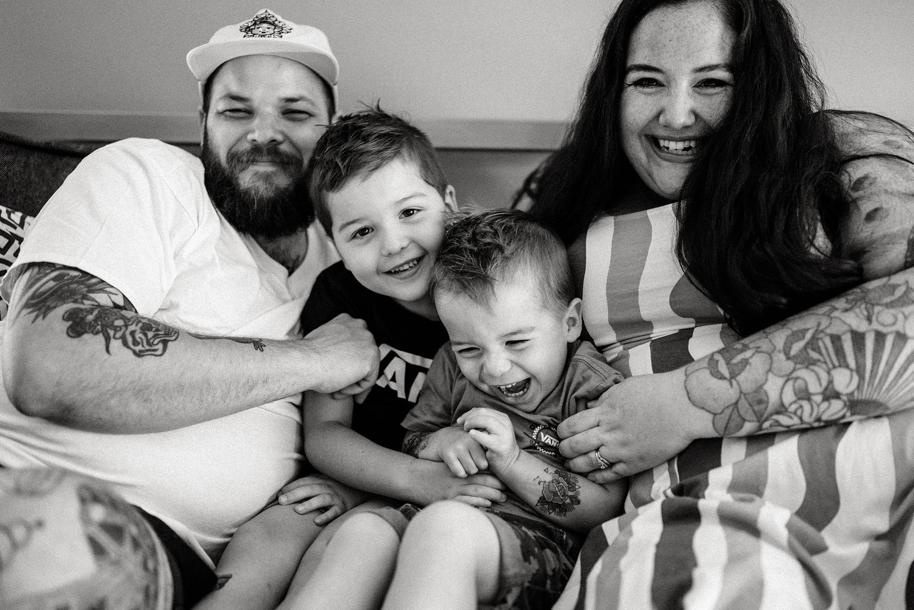 A family laughs and cuddles on a bed during their boston in home family photography session