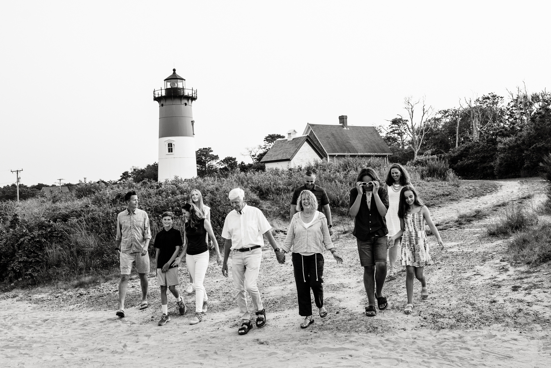 A large family laughs and walks in black and white in front of the Nauset Lighthouse in Eastham Massachusetts