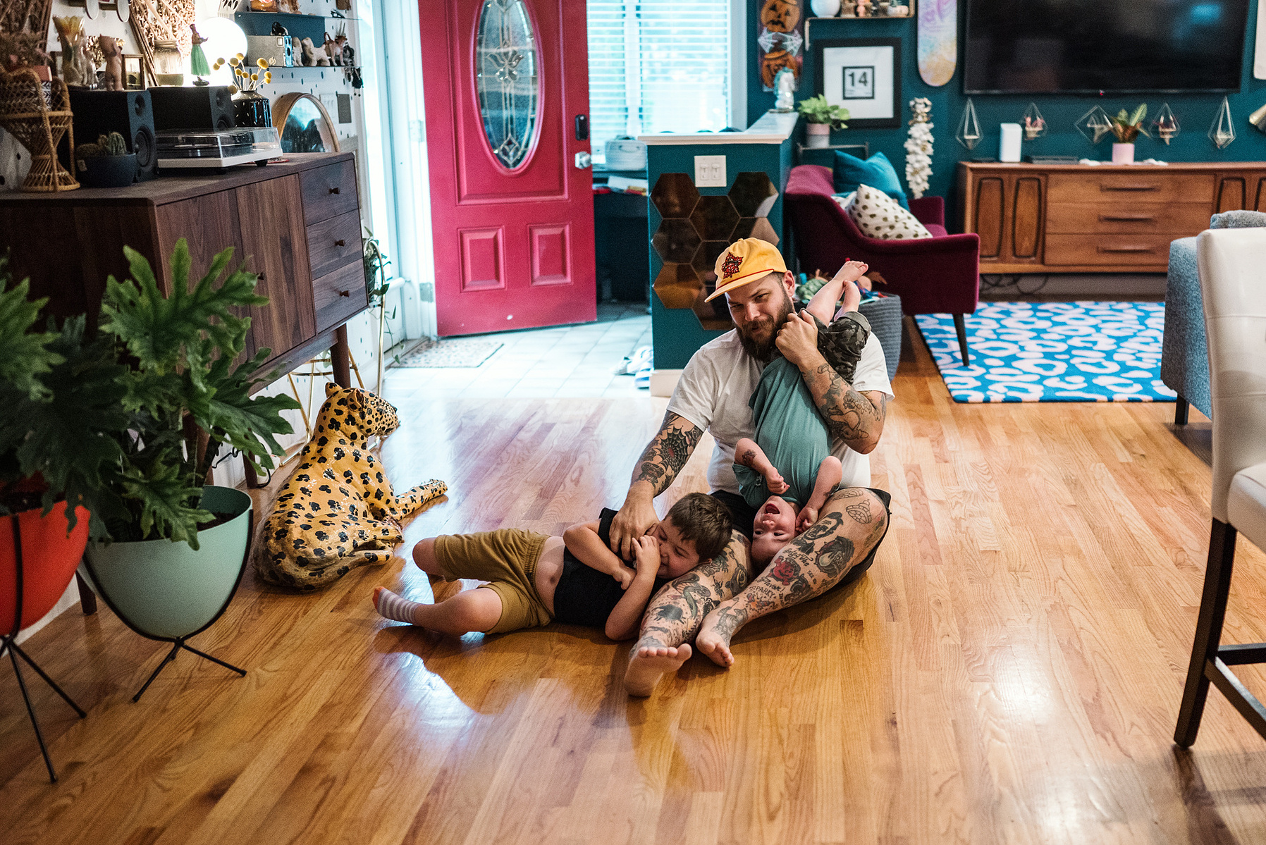 A tattooed Dad plays with his kids on the floor during their in home documentary family photoshoot in boston