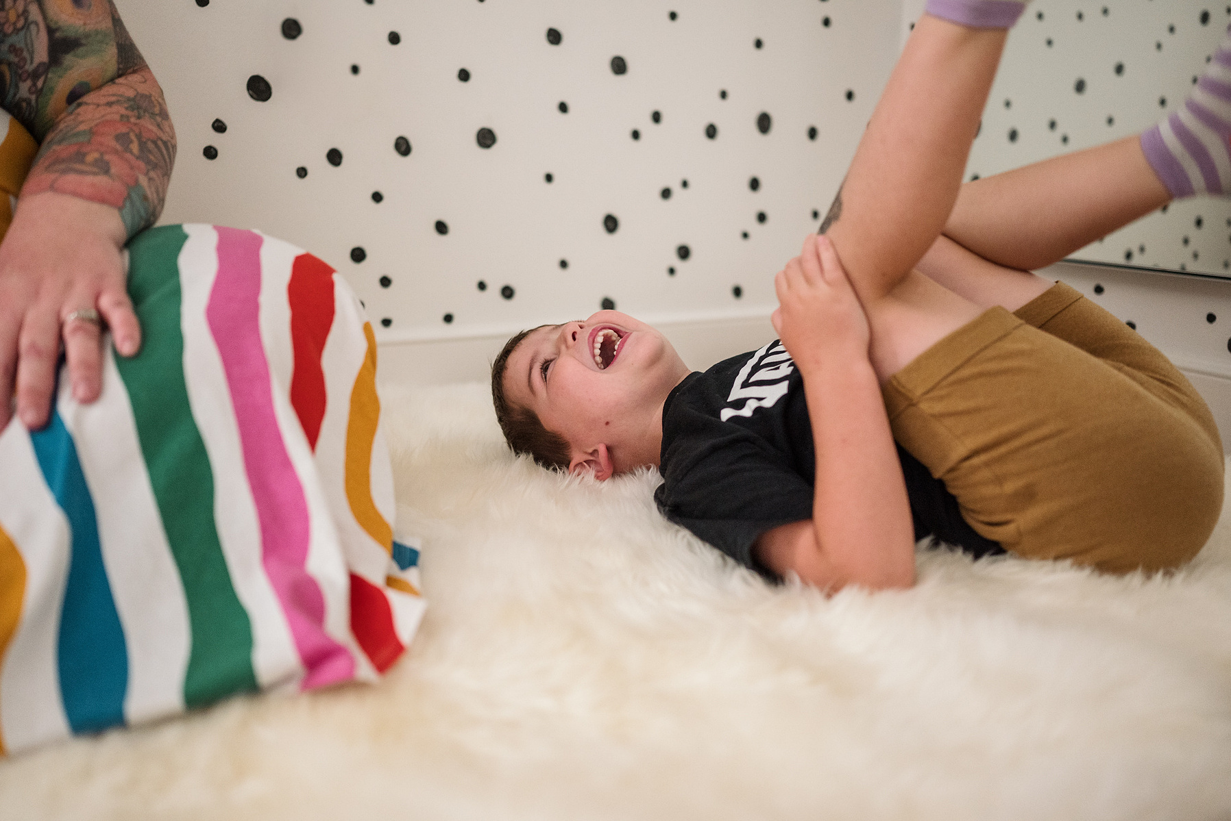 A young boy lays on the floor and laughs during their boston in home family photography session